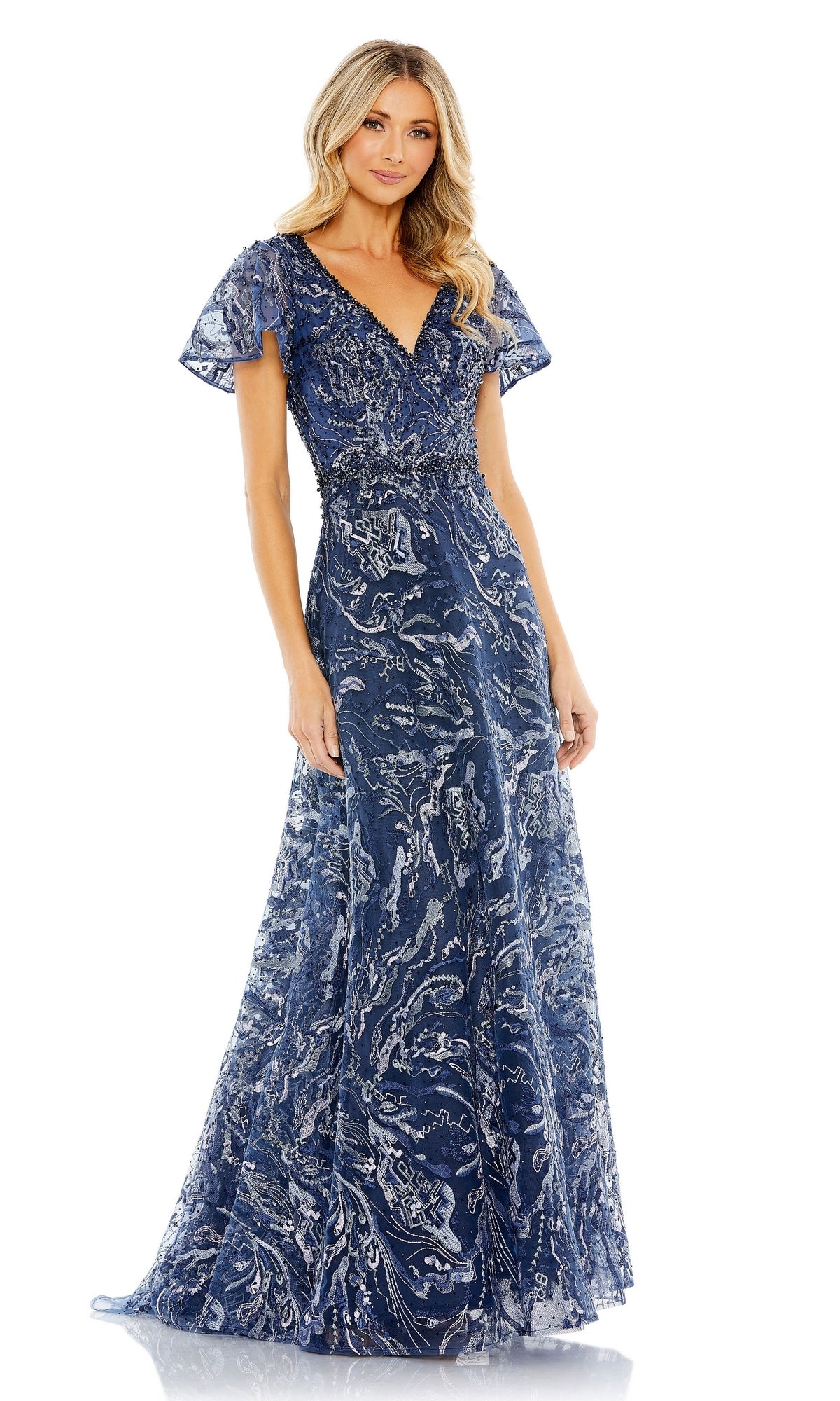 A woman wears the Mac Duggal 20301 short-sleeve formal dress, a floor-length blue A-line gown with flutter sleeves, silver detailing, and a beaded waist, posing against a plain white background.